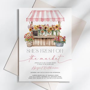 Puede incluir: Una ilustración de acuarela de un puesto de flores con un toldo a rayas rosa y blanco. El texto "She's Fresh Off the Market" está escrito en cursiva rosa. La invitación es para una despedida de soltera para Abigail Hutchinson. La fecha, la hora y la ubicación se enumeran debajo del texto.