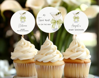 Peut inclure: Trois cupcakes blancs avec un glaçage vert et blanc. Chaque cupcake est surmonté d'un rond de papier blanc avec une illustration de verre à martini et du texte. Les toppers indiquent "Welcome Baby Hutchinson", "A Tiny One Is On The Way", et "Abigail's Baby Shower".