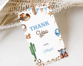 Könnte beinhalten: Ein weißes Dankeschön-Etikett mit einem blauen und braunen Cowboy-Motiv. Das Etikett zeigt einen Cowboyhut, Stiefel, ein Lasso, einen Kaktus, ein Schaukelpferd und Sterne. Der Text auf dem Etikett lautet "Danke" in braunen Buchstaben und "Liebe, Abigail" in blauen Buchstaben.