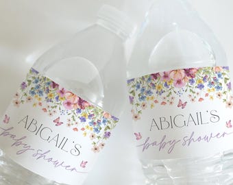 Op de afbeelding: Twee doorzichtige plastic waterflessen met bloemmotieven op de etiketten. De etiketten hebben de tekst "Abigail's baby shower" in paarse en zwarte letters.