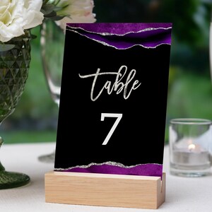 May include: Black table number card with silver glitter and purple accents. The card reads "Table 7".