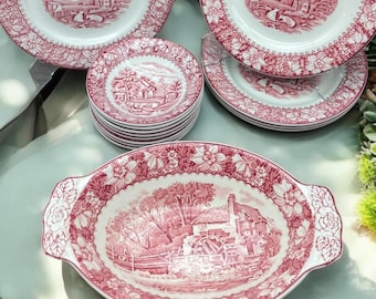 May include: A collection of vintage red and white ceramic dishes. The set includes plates of various sizes and an oval serving dish. Each piece features a scenic landscape design and floral border.