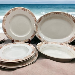 May include: Set of four white ceramic dishes with gold and brown trim. The set includes a large oval serving dish, a smaller oval dish, and two round bowls.