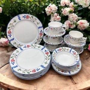 May include: A set of white ceramic dinnerware with blue and green floral designs. The set includes plates, bowls, and teacups.
