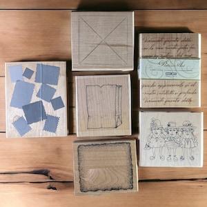 May include: A set of ten wooden rubber stamps with various designs. The stamps feature a grid pattern, a bag, a group of women with hats, and a collection of small squares. The stamps are made of wood and have a natural finish.
