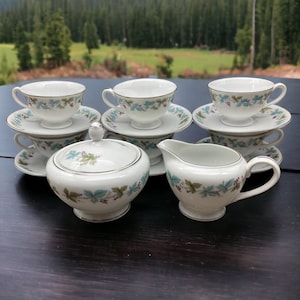 May include: A set of white teacups and saucers with a floral design, including a creamer and sugar bowl.