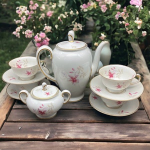 May include: A white porcelain tea set with pink floral designs and gold accents. The set includes a teapot, creamer, sugar bowl, and two teacups and saucers.
