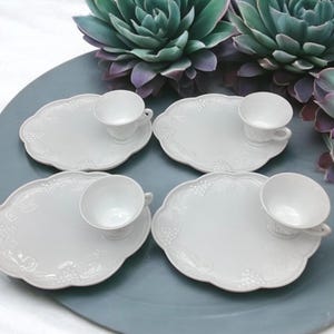 May include: Four white ceramic snack plates with matching cups. Each plate has a raised grape design and a scalloped edge.