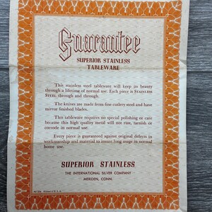 May include: A vintage guarantee card for Superior Stainless Tableware. The card features an ornate orange border and text in a classic font. The text includes a guarantee of the tableware's quality and durability, and the manufacturer's information.