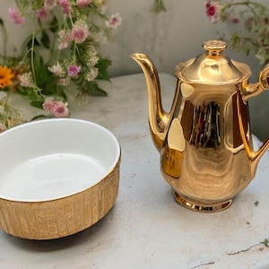 May include: A gold-plated teapot and a small bowl with a gold rim and pattern. Both are made of ceramic.