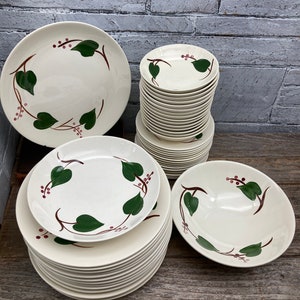 May include: A set of vintage white ceramic dinnerware with a green leaf and red berry design. The set includes a large dinner plate, a smaller salad plate, and a bowl.