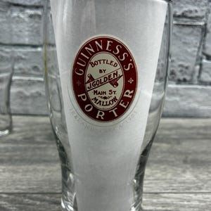 K&ouml;nnte beinhalten: Klares Pintglas mit dem Guinness's Porter Logo in Rot und Wei&szlig;. Das Logo enth&auml;lt den Text "Bottled by J. Golden, Main St. Mallow, Ireland, CA 1903". Das Glas ist teilweise mit wei&szlig;em Papier gef&uuml;llt.