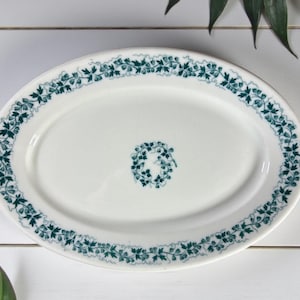 May include: Oval white serving platter with a teal floral vine pattern around the rim and a smaller floral design in the center. The platter is made of ceramic or porcelain and is suitable for serving food.