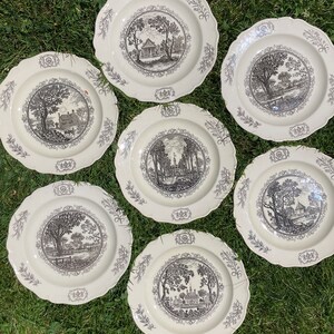 May include: Set of six white ceramic plates with black and white illustrations of houses and trees. The plates have a scalloped edge and a decorative border.