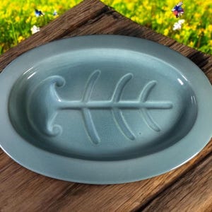 May include: A light blue ceramic serving dish with a fish bone design. The dish is oval shaped and has a raised rim.