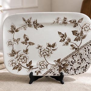 May include: Rectangular serving platter with a cream-colored background and a brown floral design. The platter features a border of small flowers and leaves. The floral pattern is arranged around the edges.
