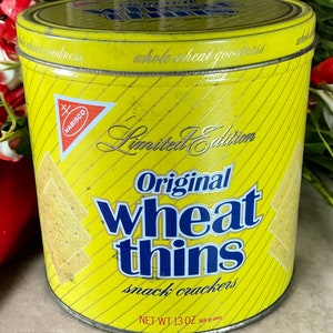May include: A yellow tin can with a red and white Nabisco logo. The can has a picture of wheat thins crackers and the text "Limited Edition Original wheat thins snack crackers NET WT 13 OZ 369 grams".