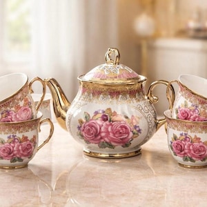 May include: A vintage tea set featuring a teapot and four teacups. The set is white with pink roses and gold trim. The teapot has a lid and a curved spout. The teacups have gold handles. The set is displayed on a marble surface.