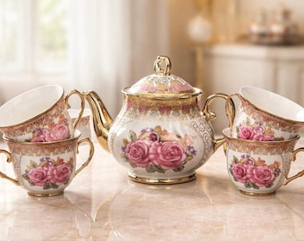 May include: A vintage tea set featuring a teapot and four teacups. The set is white with pink roses and gold trim. The teapot has a lid and a curved spout. The teacups have gold handles. The set is displayed on a marble surface.