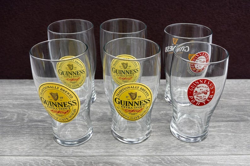 K&ouml;nnte beinhalten: Sechs klare Pintgl&auml;ser mit dem Guinness-Logo. Die Gl&auml;ser haben eine gebogene Form und einen breiten Boden. Das Guinness-Logo ist ein gold-schwarzes Etikett mit den Worten "Guinness Extra Stout" und einem Harfensymbol.