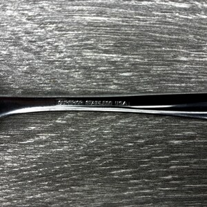 May include: Close-up of a stainless steel fork with the text "SUPERIOR STAINLESS USA" etched on the handle. The fork is set against a textured, gray wooden surface.