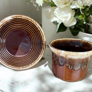 May include: A set of two brown and white ceramic bowls with a glazed finish. The larger bowl has a concentric circle design and the smaller bowl has a drip glaze pattern.