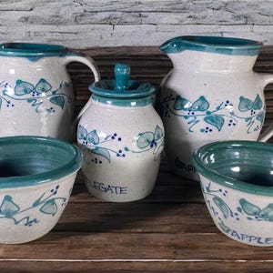 May include: Set of five white ceramic kitchenware pieces with a blue and green floral design. The set includes two pitchers, a jar, and two bowls. The jar is labeled "Legate".