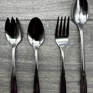 May include: Four-piece stainless steel flatware set. Includes a salad fork, a spoon, a dinner fork, and a serving spoon. The handles have a dark, reddish-brown color, and the utensils are arranged on a gray wooden surface.