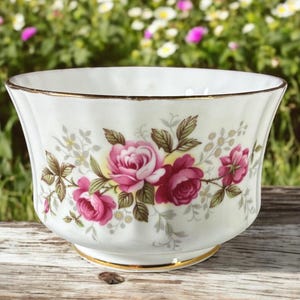 May include: A white porcelain sugar bowl with a gold rim and a floral pattern of pink roses and green leaves.