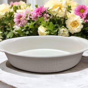May include: White ceramic pie plate with a fluted edge and two handles. The plate is sitting on a white surface.