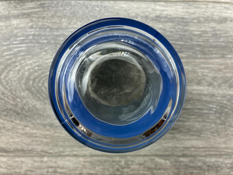 May include: A clear glass with a blue rim, viewed from above. The glass is empty, and the blue rim creates a distinct border around the opening. The glass sits on a gray wooden surface.