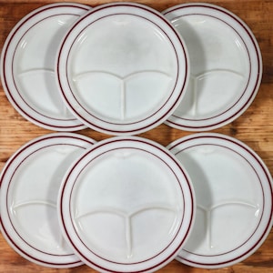 May include: Six white divided plates with a maroon rim. The plates are divided into three sections.