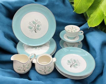 May include: A vintage tea set featuring plates, saucers, cups, a creamer, and a sugar bowl. The set has a light blue border with a white center, adorned with a tree design. The set is made of ceramic.
