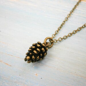 May include: A gold chain necklace with a small, detailed pine cone pendant.