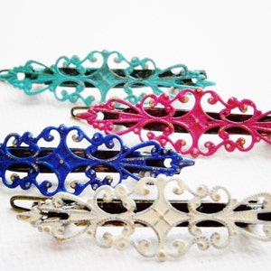 Könnte beinhalten: Vier dekorative Haarklammern in verschiedenen Farben. Die Klammern sind aus Metall und haben ein filigranes Design. Die Farben sind Türkis, Rosa, Blau und Weiß.