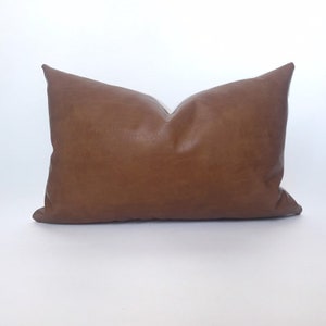 May include: A brown leather lumbar pillow with a smooth, textured surface.