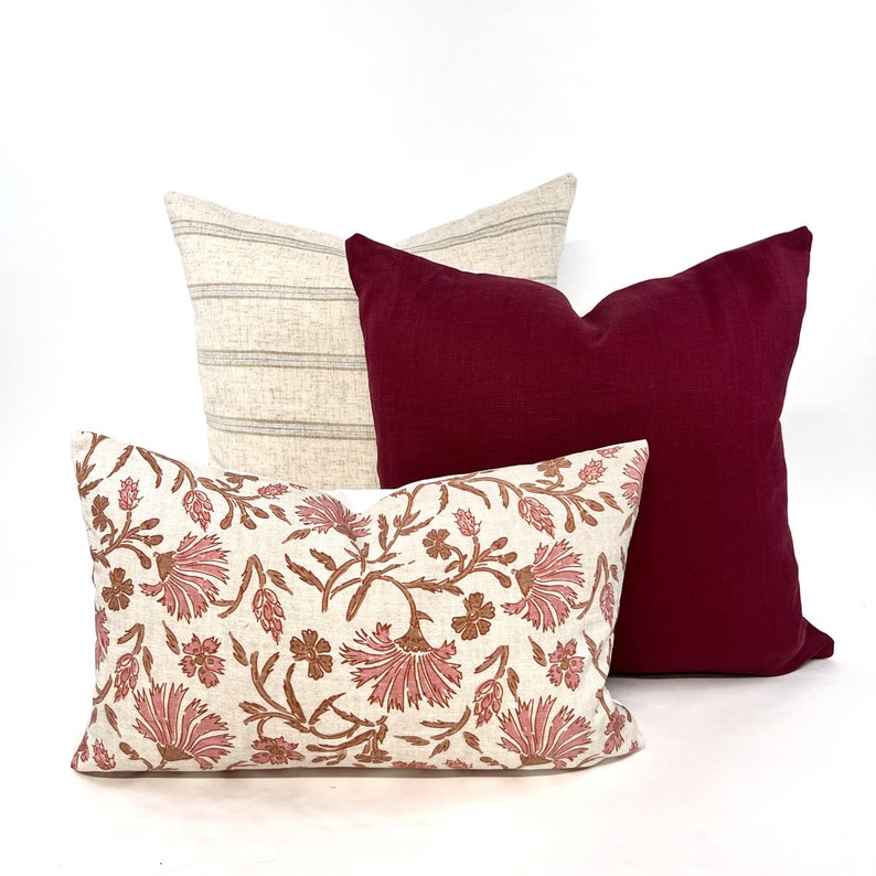 Op de afbeelding: Drie decoratieve kussens. Een kussen is cr&egrave;mekleurig met een bruin en wit gestreept patroon. Een ander kussen is donker bordeauxrood. Het derde kussen is cr&egrave;mekleurig met een bloemenpatroon in bruine en roze tinten.