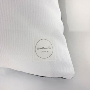 May include: White pillow with a black border and a white label with the text "Cotton+Co. Spokane, WA" in black.