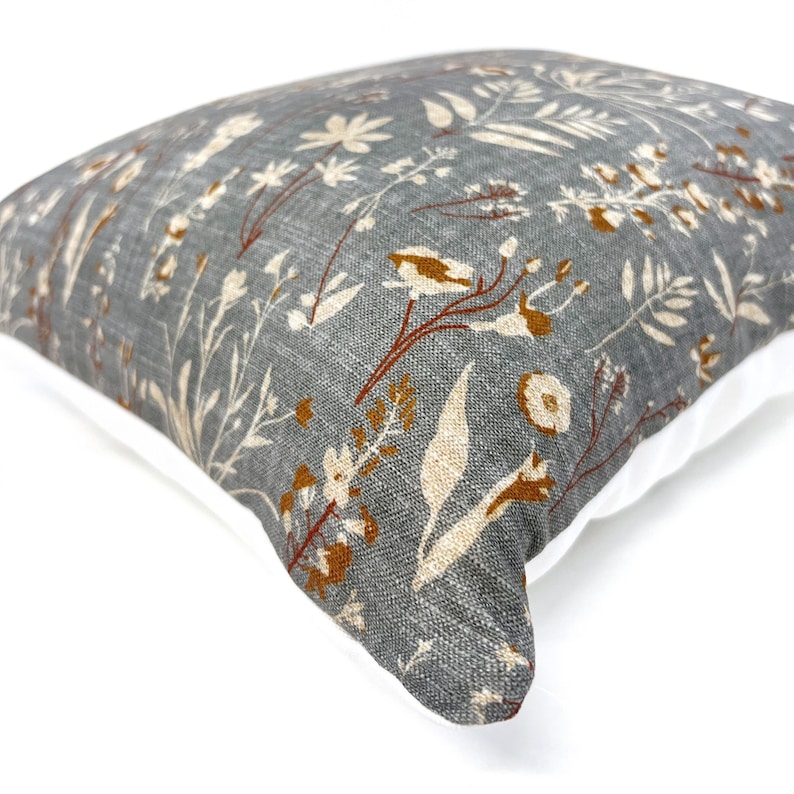 May include: A gray throw pillow with a white and brown floral pattern. The pillow has a white border.