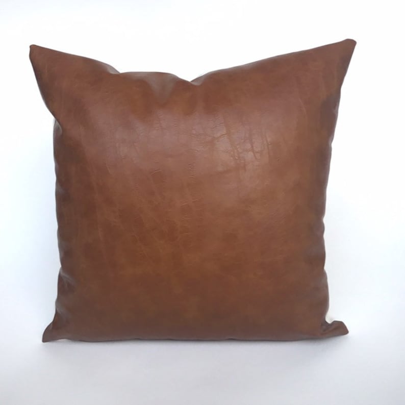 May include: A brown leather pillow with a square shape. The pillow is made of a soft, textured material.