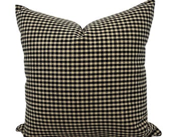 Puede incluir: Un cojín decorativo cuadrado con un patrón de cuadros vichy en negro y crema. El cojín tiene un aspecto suave y afelpado y está diseñado para la decoración del hogar. La tela tiene un diseño clásico a cuadros.