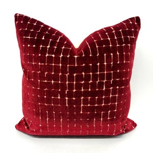 May include: A square decorative pillow with a deep red velvet fabric. The pillow features a grid pattern of small, off-white squares. The pillow is a square shape and is likely used for home decor.