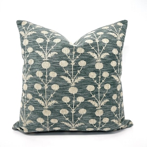 May include: A teal blue throw pillow with a white floral pattern. The pillow features a repeating design of stylized white flowers with stems on a teal blue background.