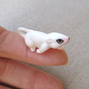 Op de afbeelding: Een kleine, witte plastic eekhoornfiguur met een roze neus en zwarte ogen. Het miniatuurdier heeft een gebogen staart en kruipt. Het beeldje is een knutselbenodigdheid of een decoratief item.
