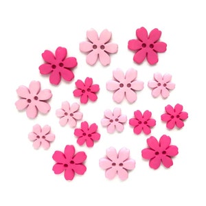 May include: A collection of flower-shaped buttons in varying shades of pink, from light to hot pink. Each button has two holes for sewing. The buttons are scattered on a white background, showcasing their floral design.