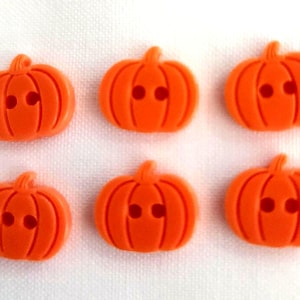 May include: A set of six bright orange pumpkin-shaped buttons arranged in two rows of three. Each button features a carved ribbed texture and two central holes for sewing, with a small stem detail at the top of each individual pumpkin shape.