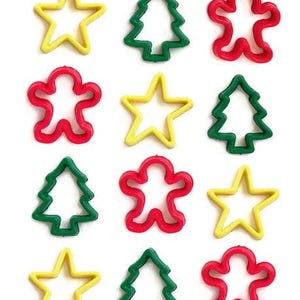May include: A collection of colorful cookie cutters in the shapes of stars, Christmas trees, and gingerbread people. The cutters are yellow, green, and red, arranged on a white background.
