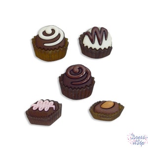 May include: Five chocolate candies in brown paper wrappers. The candies are decorated with white and brown swirls, pink swirls, and a single almond.