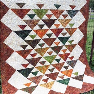 May include: A quilt with a geometric pattern of triangles in shades of brown, green, and orange. The triangles are arranged in a cascading pattern, creating a sense of movement. The quilt is made with a variety of fabrics, including batiks.
