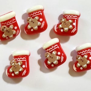 May include: Six small, glossy, red Christmas stocking-shaped charms, each featuring a white cuff, white snowflake accents, and a central light brown gingerbread man figure with white icing details, arranged in a scattered pattern.